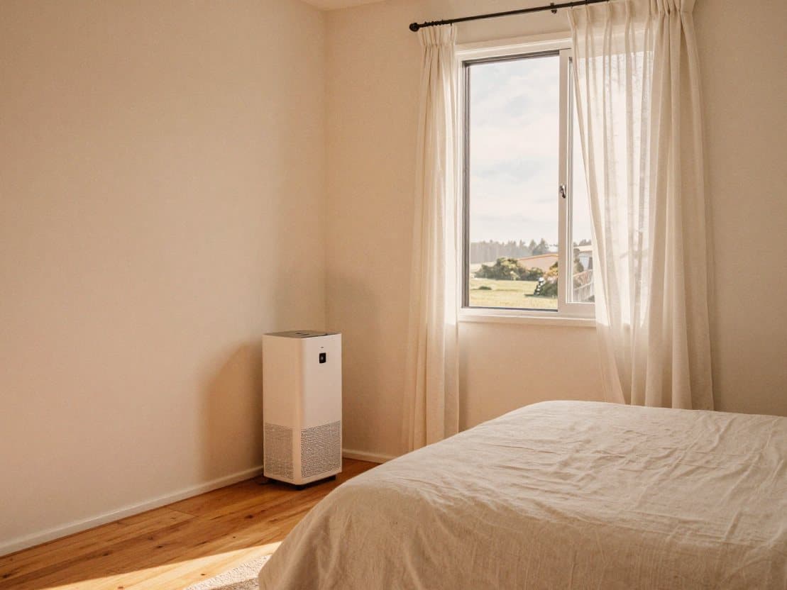 A bright bedroom with the window open and a dehumidifier in the corner