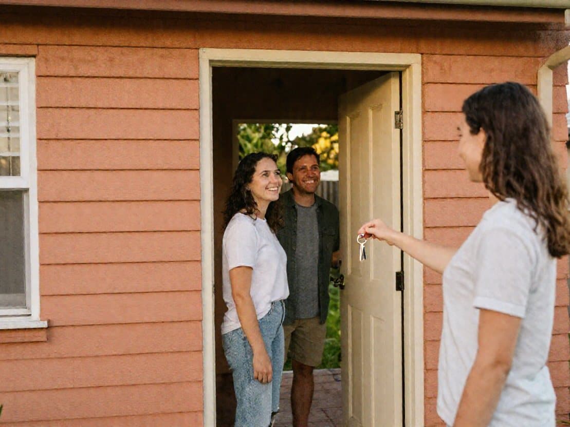 A landlord handing house keys to a couple at the front door of a weatherboard house