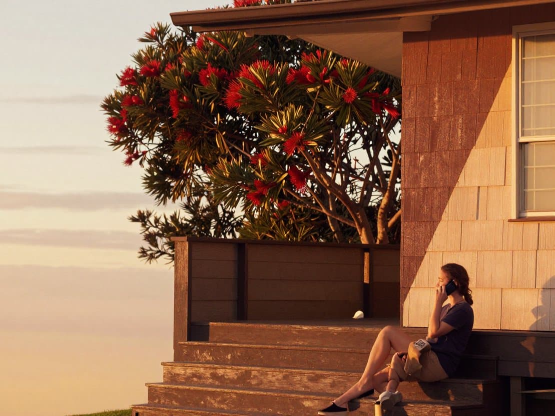 Someone sitting on the front steps of a weatherboard house, on the phone