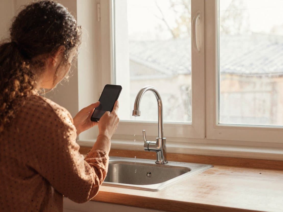 A tenant photographing a dripping kitchen tap with their phone